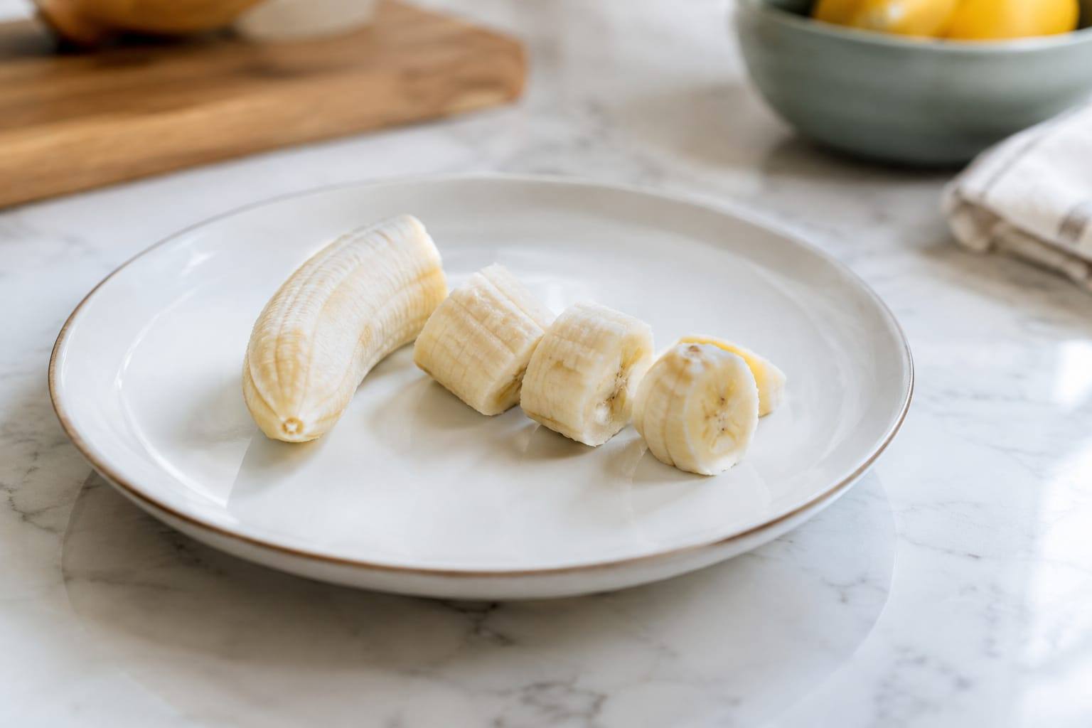 Une banane mûre, pelée et coupée en petites rondelles sur une planche propre, dans une cuisine lumineuse.