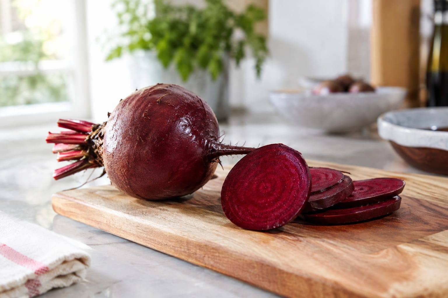 Une betterave crue lavée et quelques rondelles sont disposées sur une planche dans une cuisine lumineuse.