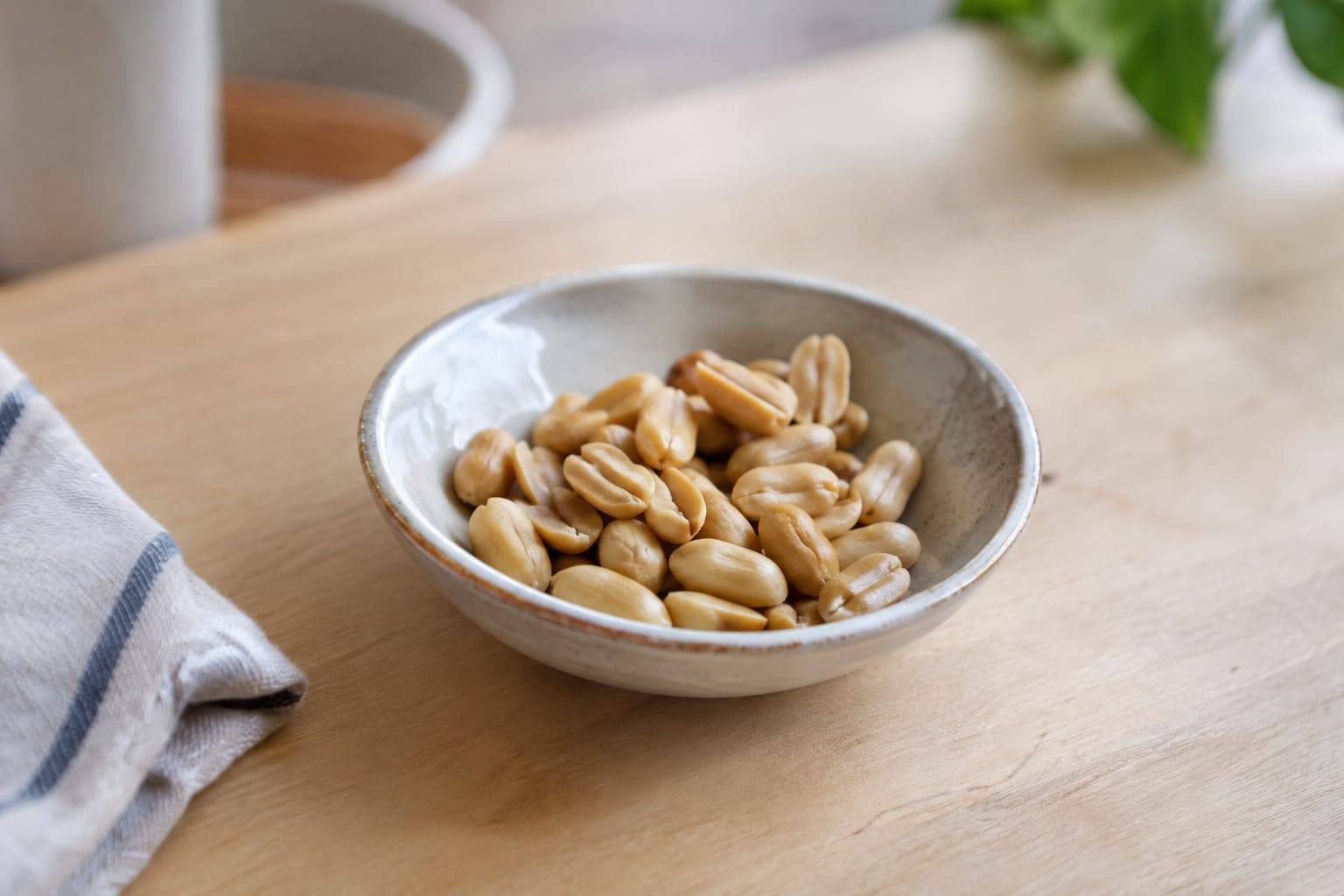 Quelques cacahuètes décortiquées, dont une moitié, posées dans une petite coupelle en céramique sur une table claire.