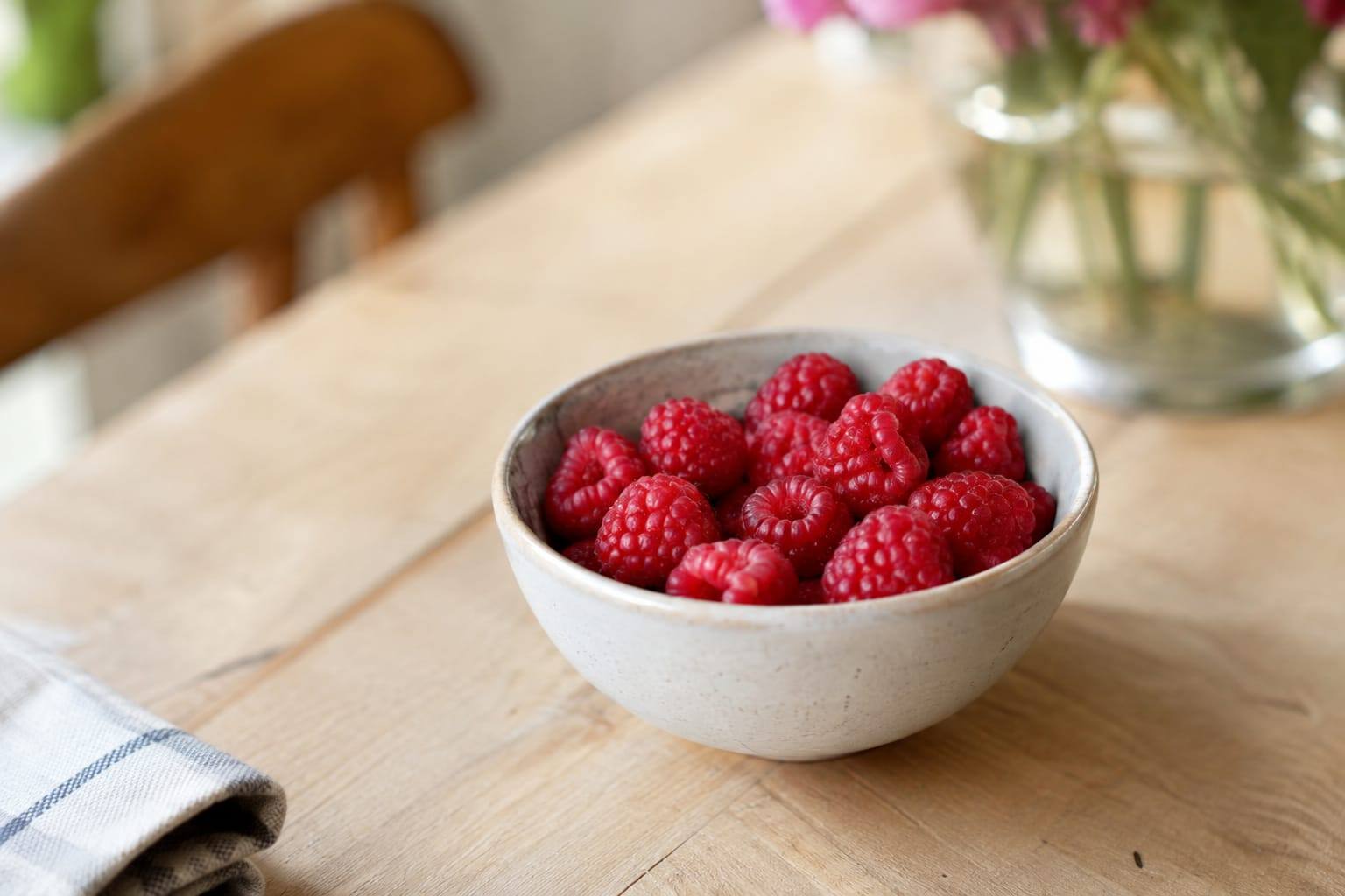 Quelques framboises fraîches, rincées et posées dans une petite coupelle en céramique sur une table claire.