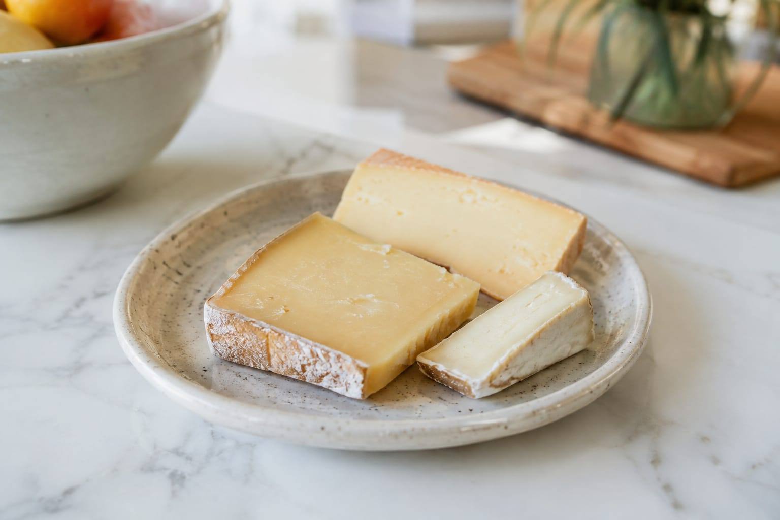 Morceaux de fromage nature sur une petite assiette, posés sur une table claire dans une cuisine.