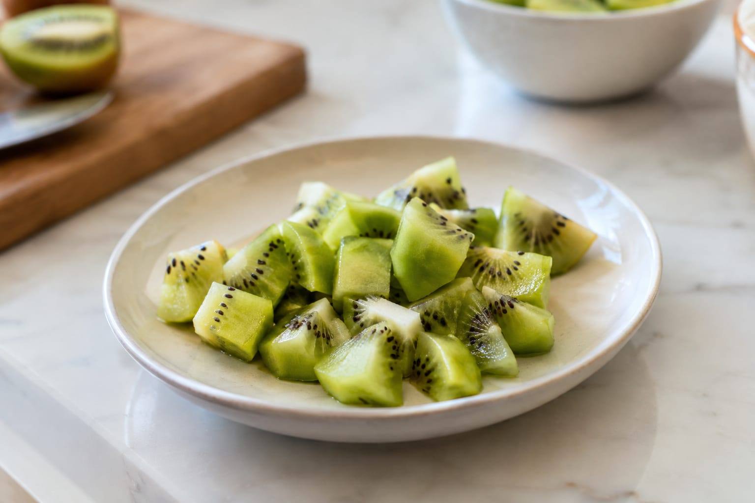Un kiwi mûr pelé et coupé en petits morceaux sur une assiette, prêt à être proposé en friandise.