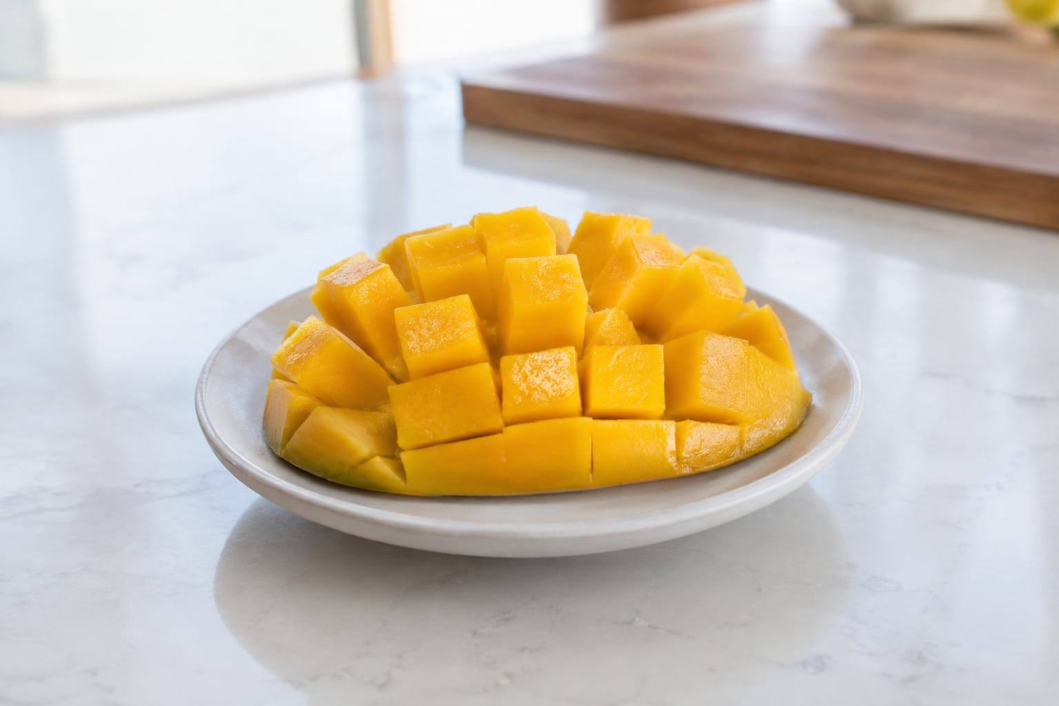 Morceaux de mangue fraîche et pelée, coupés en petits dés sur une assiette claire dans une cuisine lumineuse.