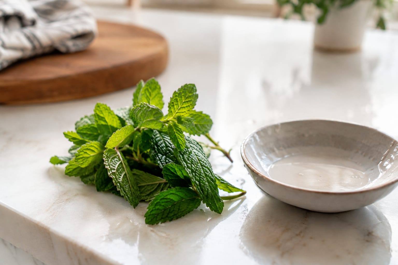 Feuilles de menthe fraîche, propres et non traitées, disposées près d’une petite coupelle dans une cuisine lumineuse.
