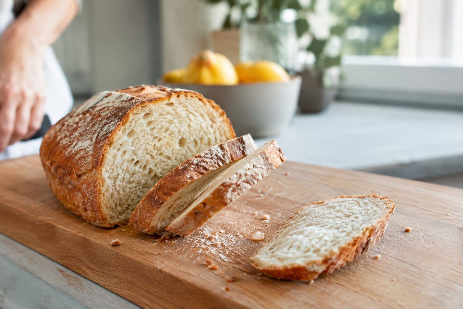 Tranches de pain nature et miettes sur une planche en bois, photographiées dans une cuisine claire, sans animal.