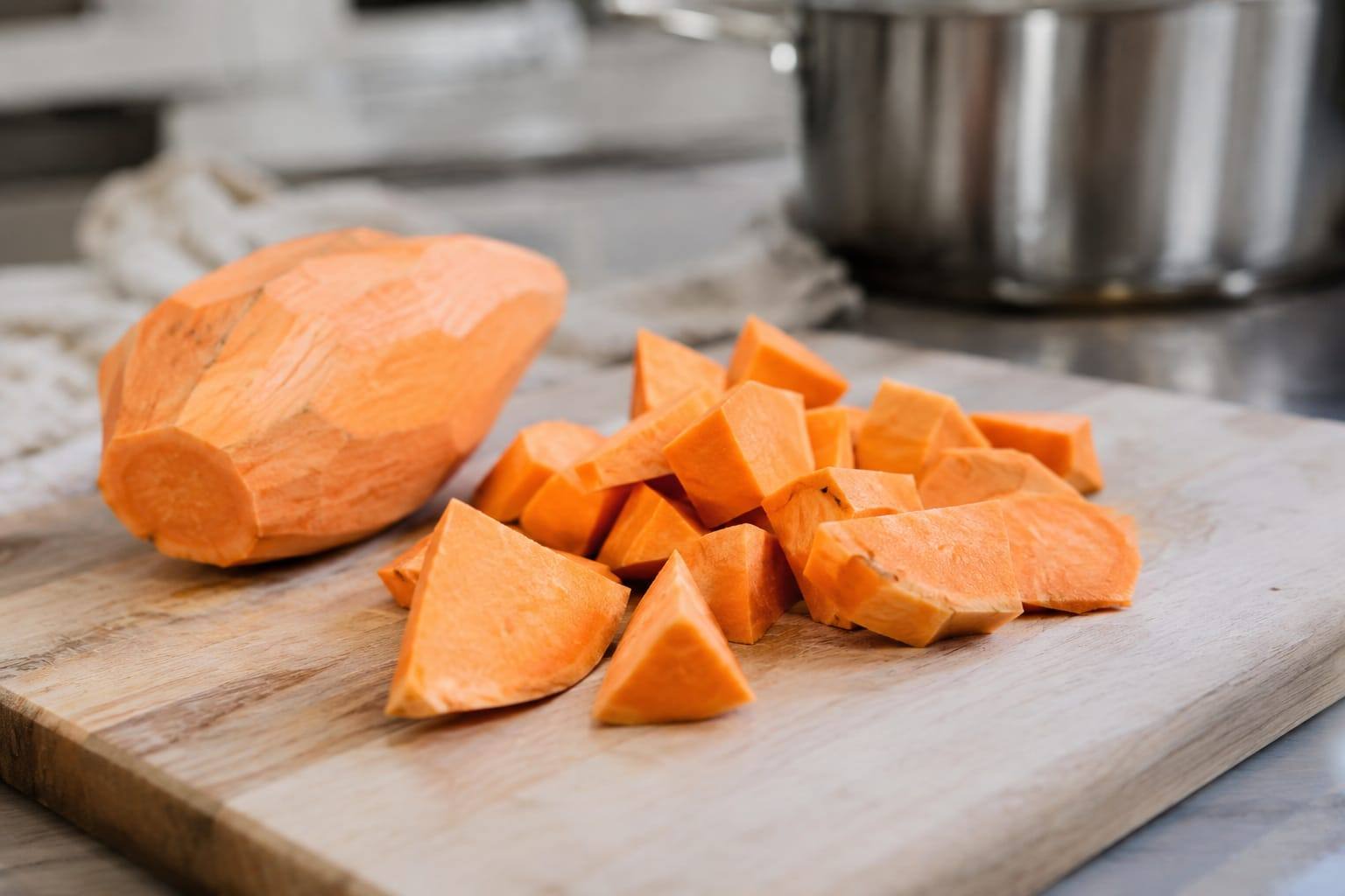 Petit morceau de patate douce fraîche et épluchée, posé sur une planche claire dans une cuisine lumineuse.