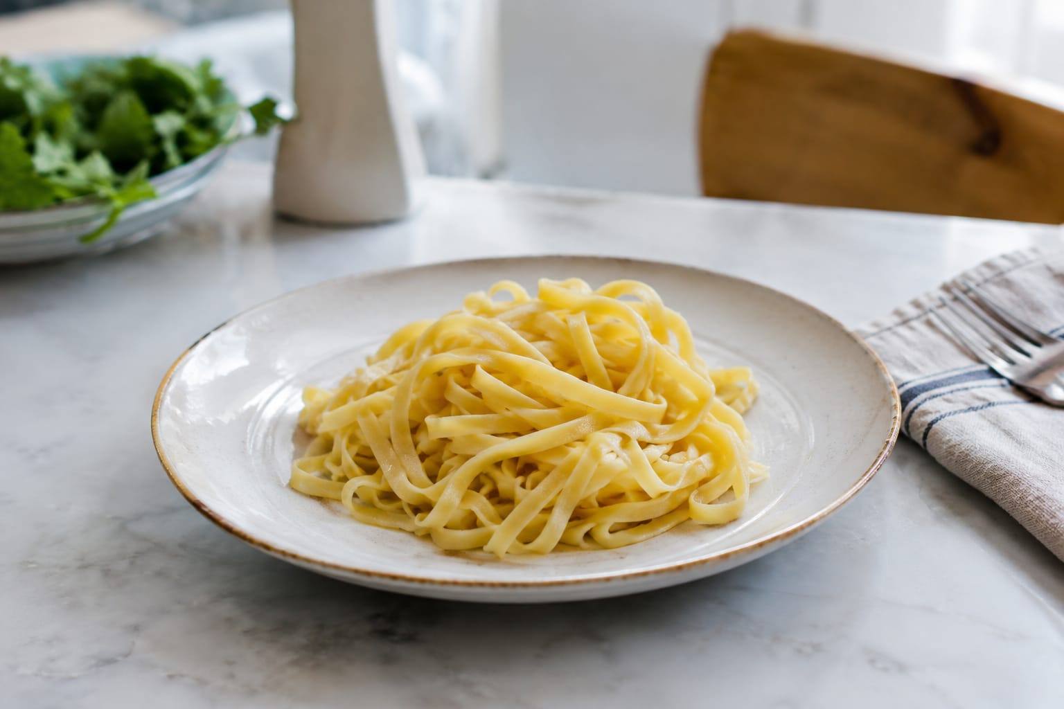 Petit morceau de pâtes nature cuites et refroidies, présenté dans une assiette claire sur une table de cuisine.