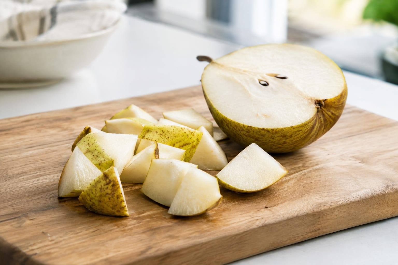 Poire coupée en petits morceaux sur une planche en bois, à côté d'une demi-poire dont on voit encore les pépins.