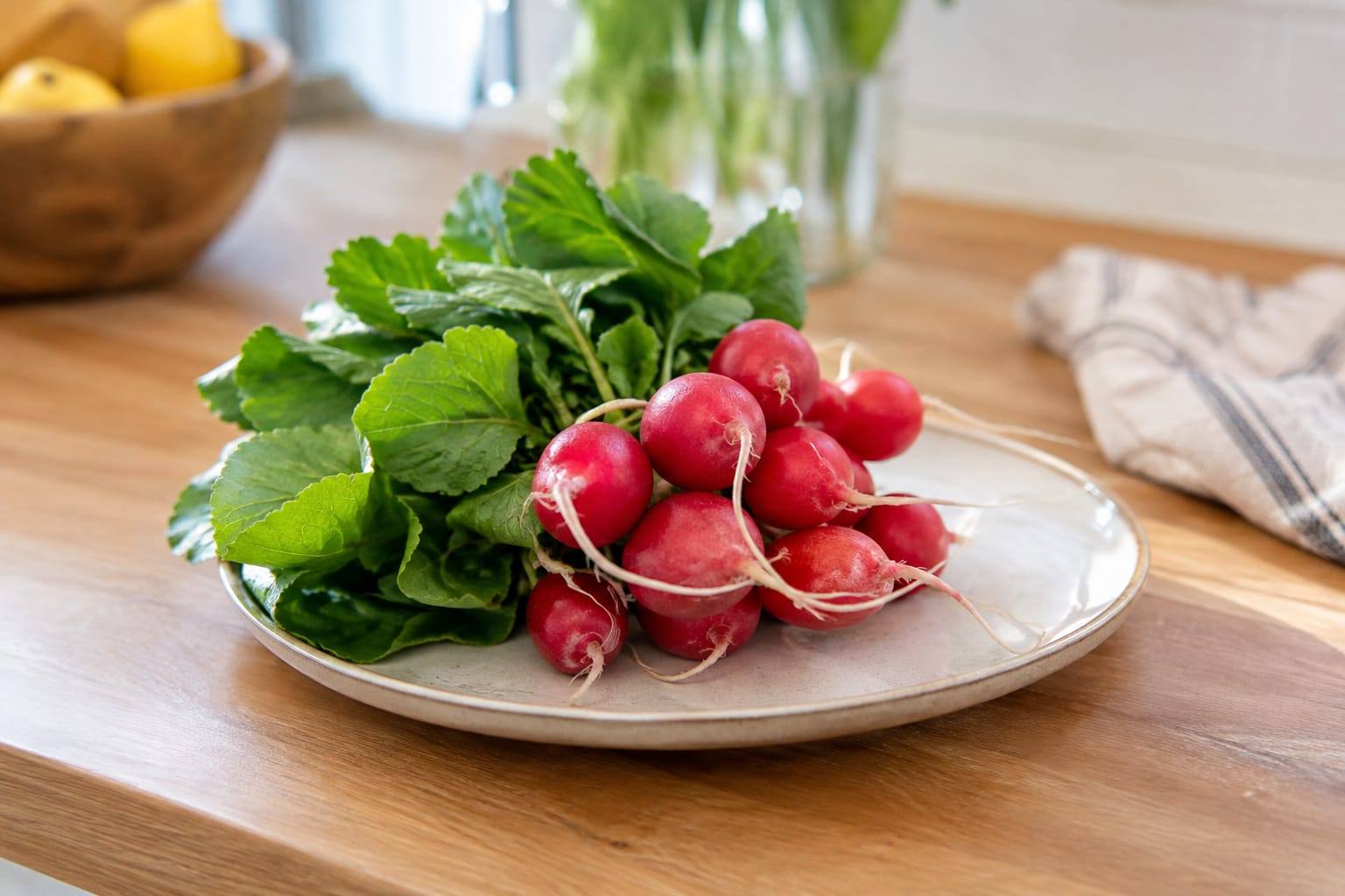 Radis rouges frais avec leurs fanes vertes, lavés et posés sur une planche dans une cuisine lumineuse.